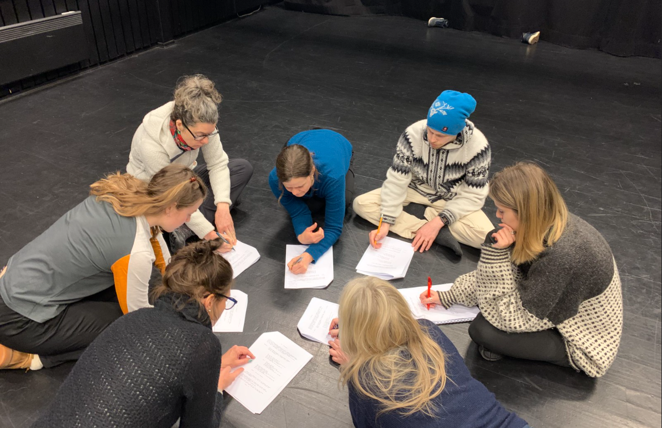 Mennesker i ring på gulvet leser tekst