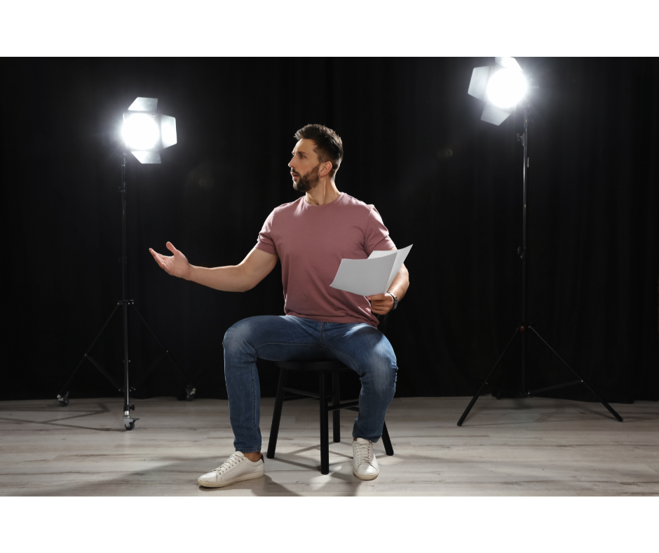 mann som sitter på en stol på en scene, tekst i en hånd