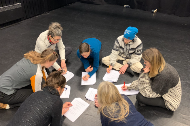 Mennesker i ring på gulvet leser tekst