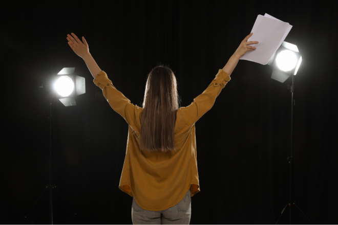 jente på scenen med armene strekt opp og en tekst i den ene hånden