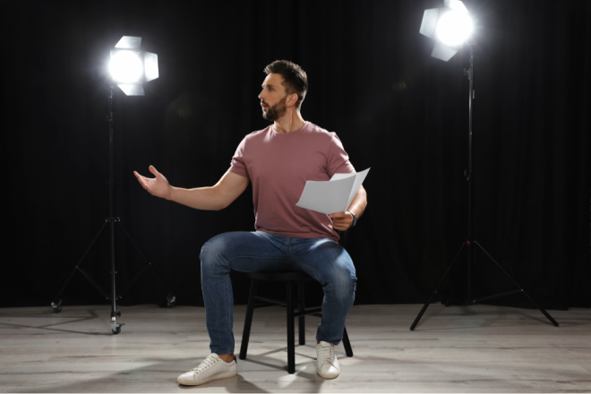 mann som sitter på en stol på en scene, tekst i en hånd
